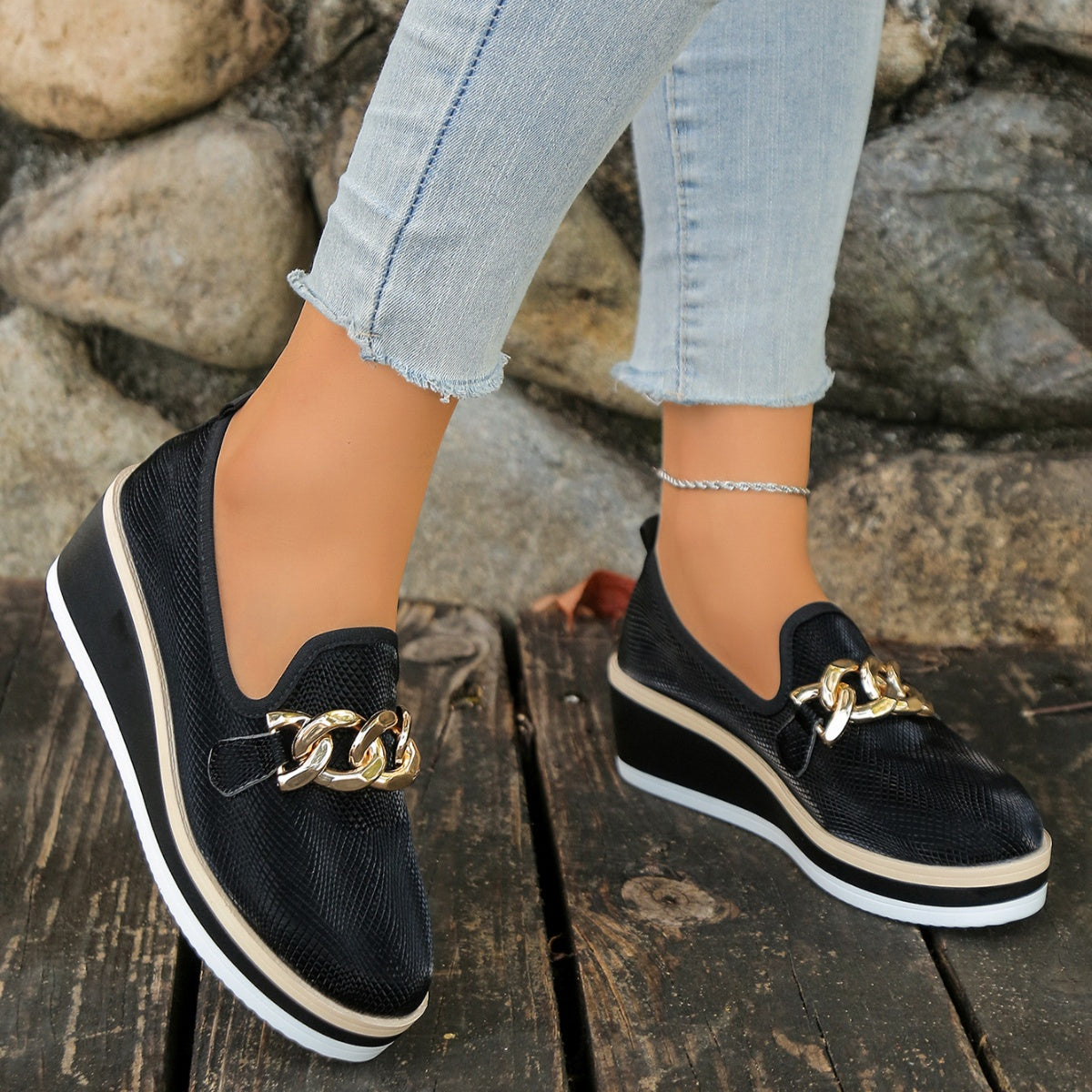Black wedge loafers with gold chain detail and layered sole.