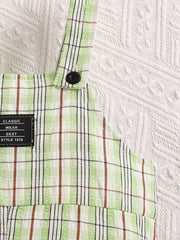 Children's green plaid overalls with adjustable straps and a black button detail.