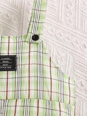 Children's green plaid overalls with adjustable straps and a black button detail.