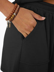 Black drawstring shorts with pockets, shown on a model wearing bracelets.
