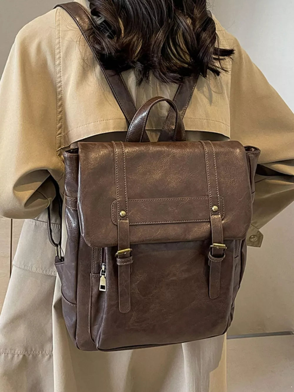 Brown pu leather flap backpack with brass hardware and adjustable straps.