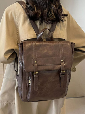 Brown pu leather flap backpack with brass hardware and adjustable straps.