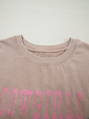 Acid-washed cotton tank top in Khaki with distressed pink "COWGIRLS" graphic.