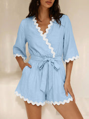 Blue wrap romper with white scalloped trim and 3/4 sleeves, tied at waist.
