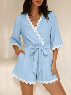 Blue wrap romper with white scalloped trim and 3/4 sleeves, tied at waist.