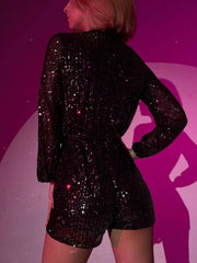 Black sequin romper with blouson sleeves and shorts, featuring a wrap front detail.