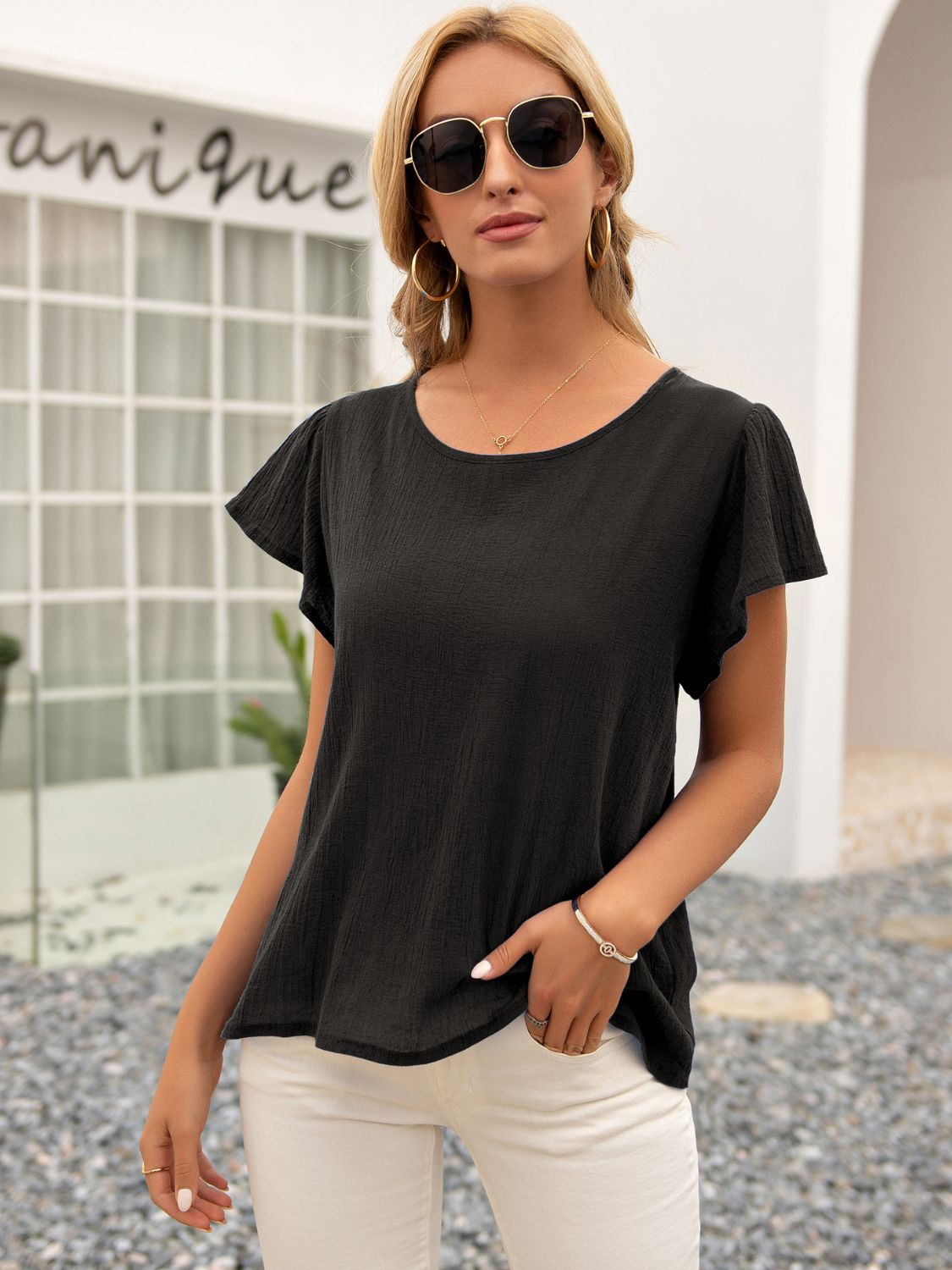 Black textured blouse with flutter sleeves and a round neckline.