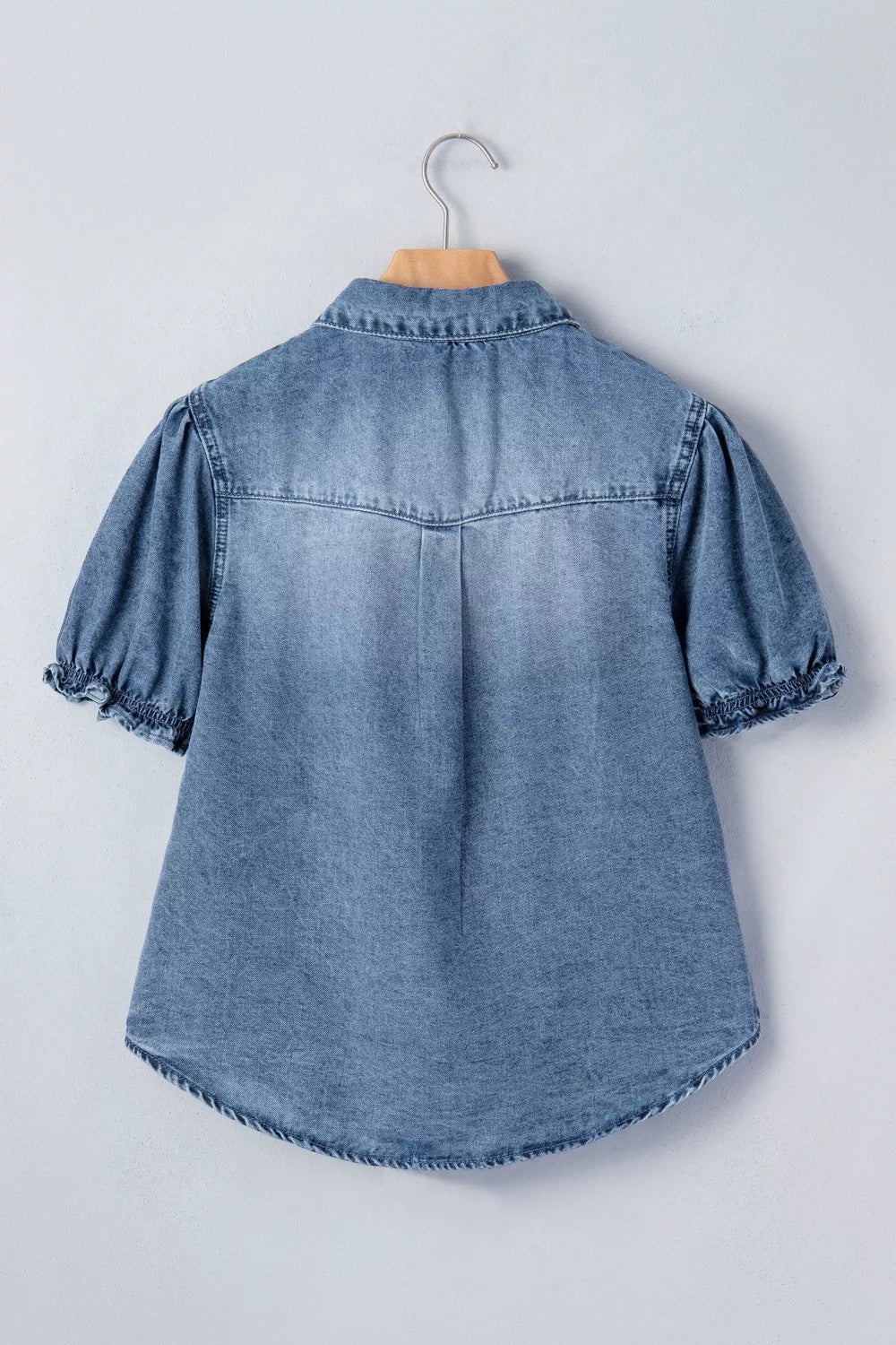 Denim shirt with short ruffled sleeves and snap closure, hanging on a hanger.