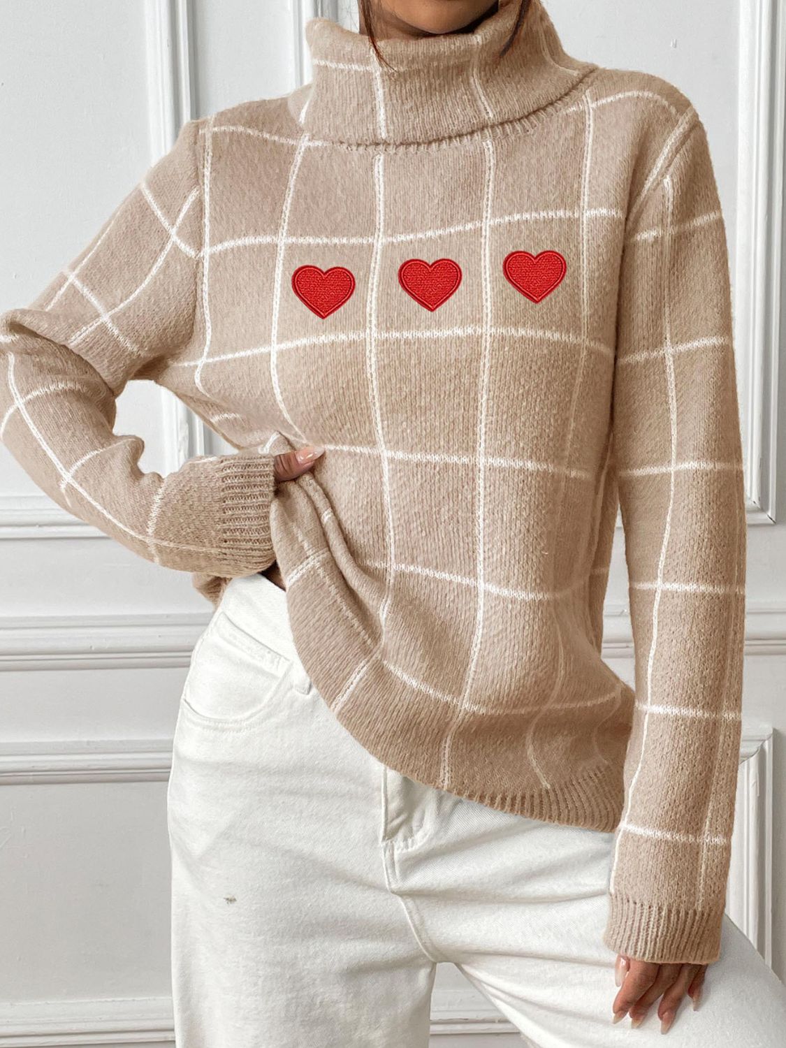 Tan gridwork turtleneck sweater with three red heart appliqués.