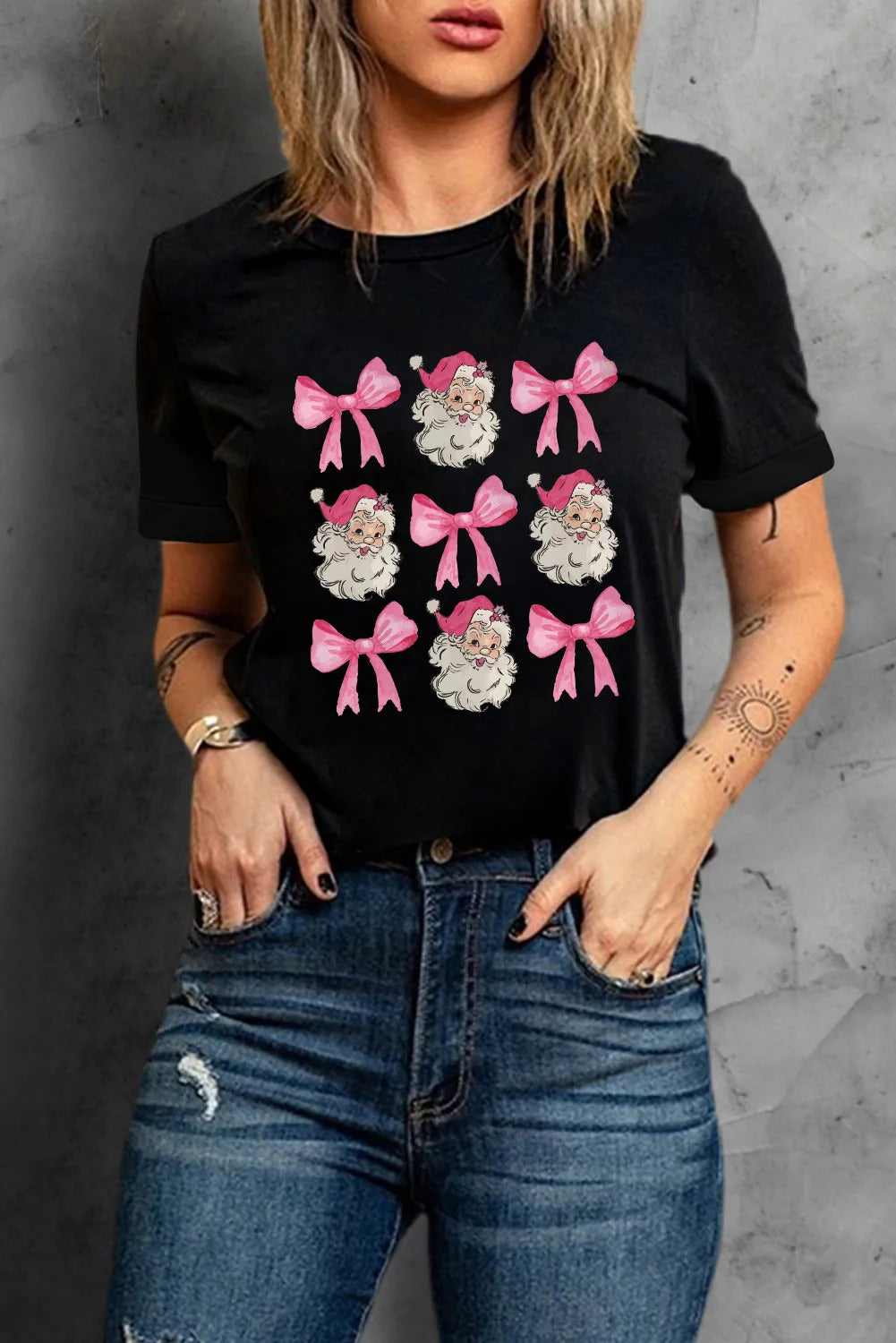 Black t-shirt with a grid of Santa faces and pink bows graphic print.