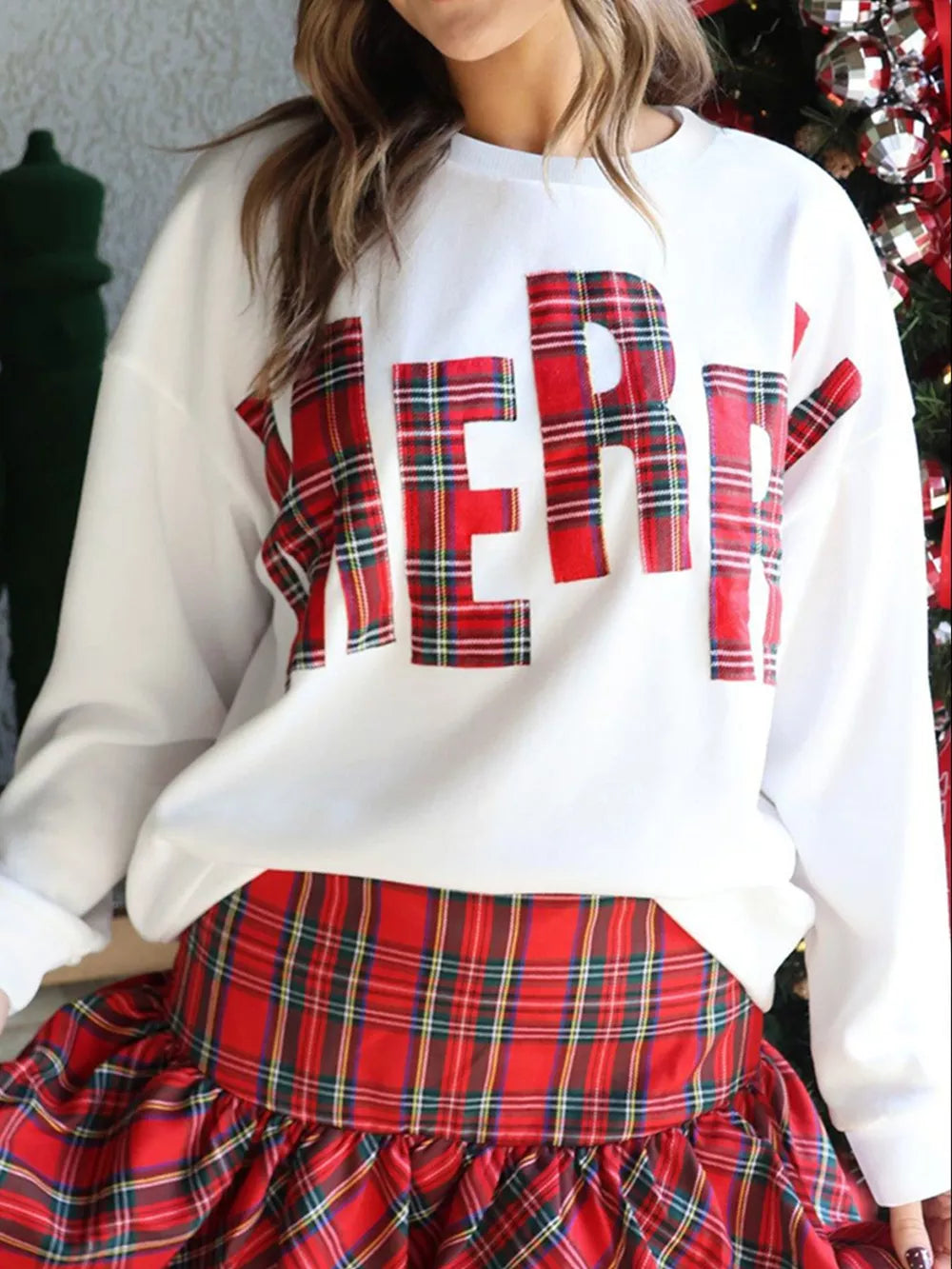 White crew neck sweatshirt with red plaid "Merry" graphic, long sleeves, cotton.
