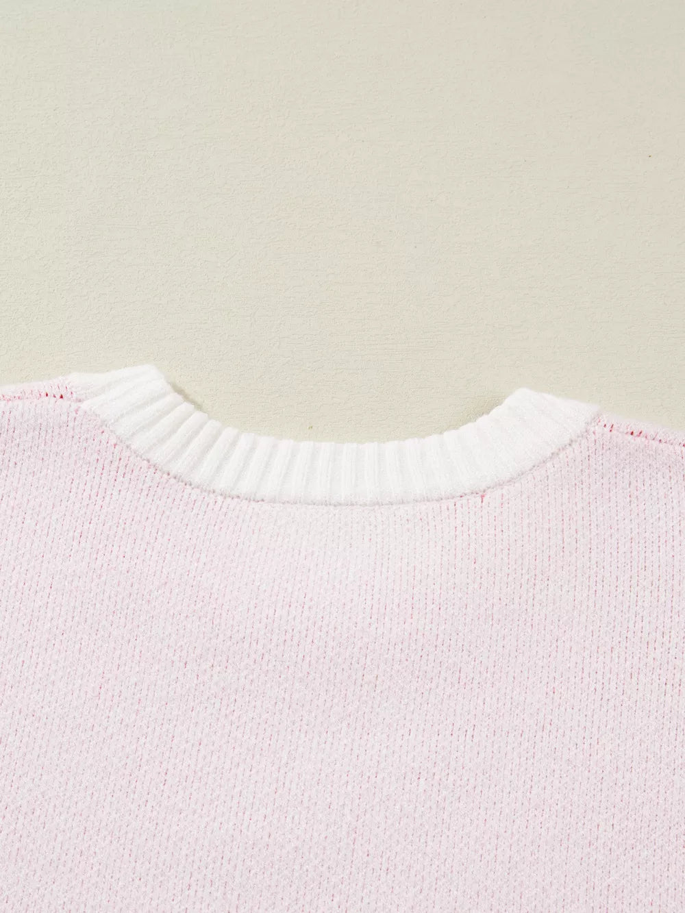 Blush pink knit sweater with white ribbed crew neck and appliqué detail.