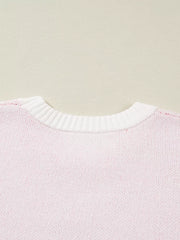 Blush pink knit sweater with white ribbed crew neck and appliqué detail.