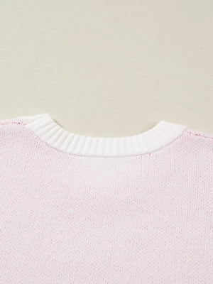 Blush pink knit sweater with white ribbed crew neck and appliqué detail.