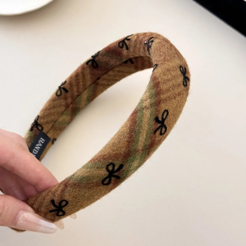 Padded headband in camel plaid with black bow embroidery and a textured fabric.