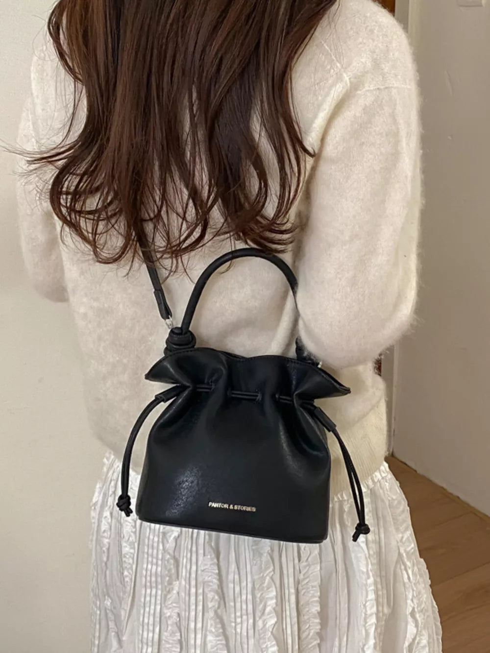 Black pu leather cinch-top crossbody bag with drawstring closure and top handle.