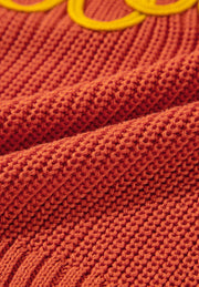 Orange knit sweater with yellow embroidered detail, showing textured acrylic fabric.