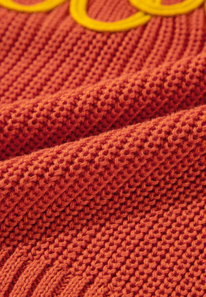 Orange knit sweater with yellow embroidered detail, showing textured acrylic fabric.