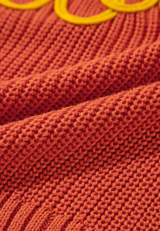 Orange knit sweater with yellow embroidered detail, showing textured acrylic fabric.