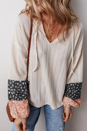 Textured sleeve henley blouse with patchwork floral cuffs and tie-neck detail.
