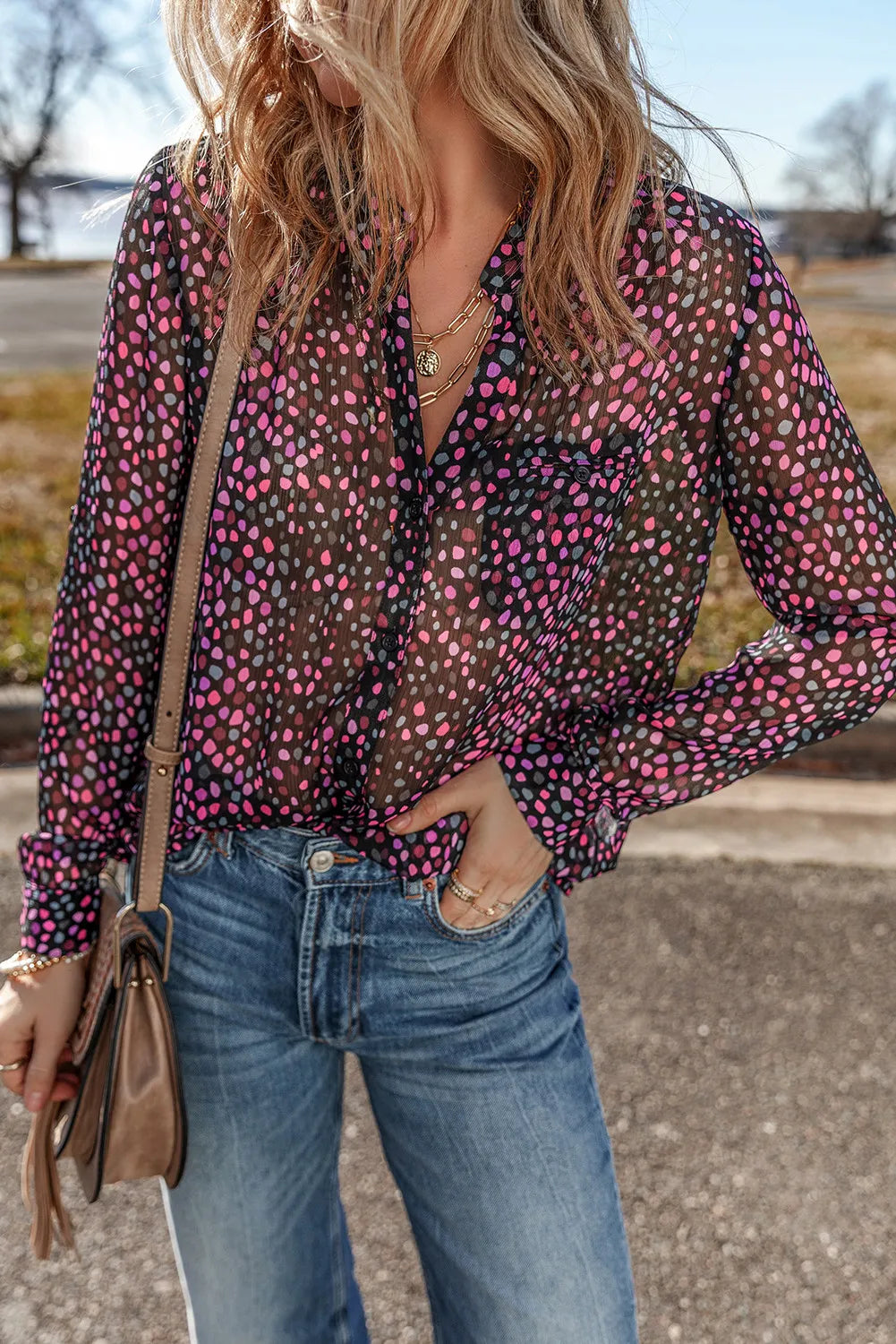 Sheer dotted blouse in black with knot detail and button cuffs, styled with jeans.