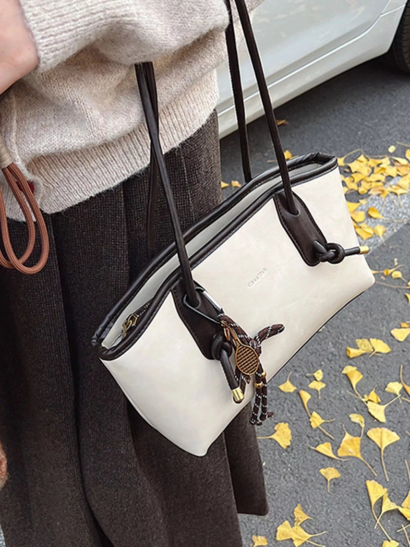White leather shoulder bag with brown trim and tennis racket charm.