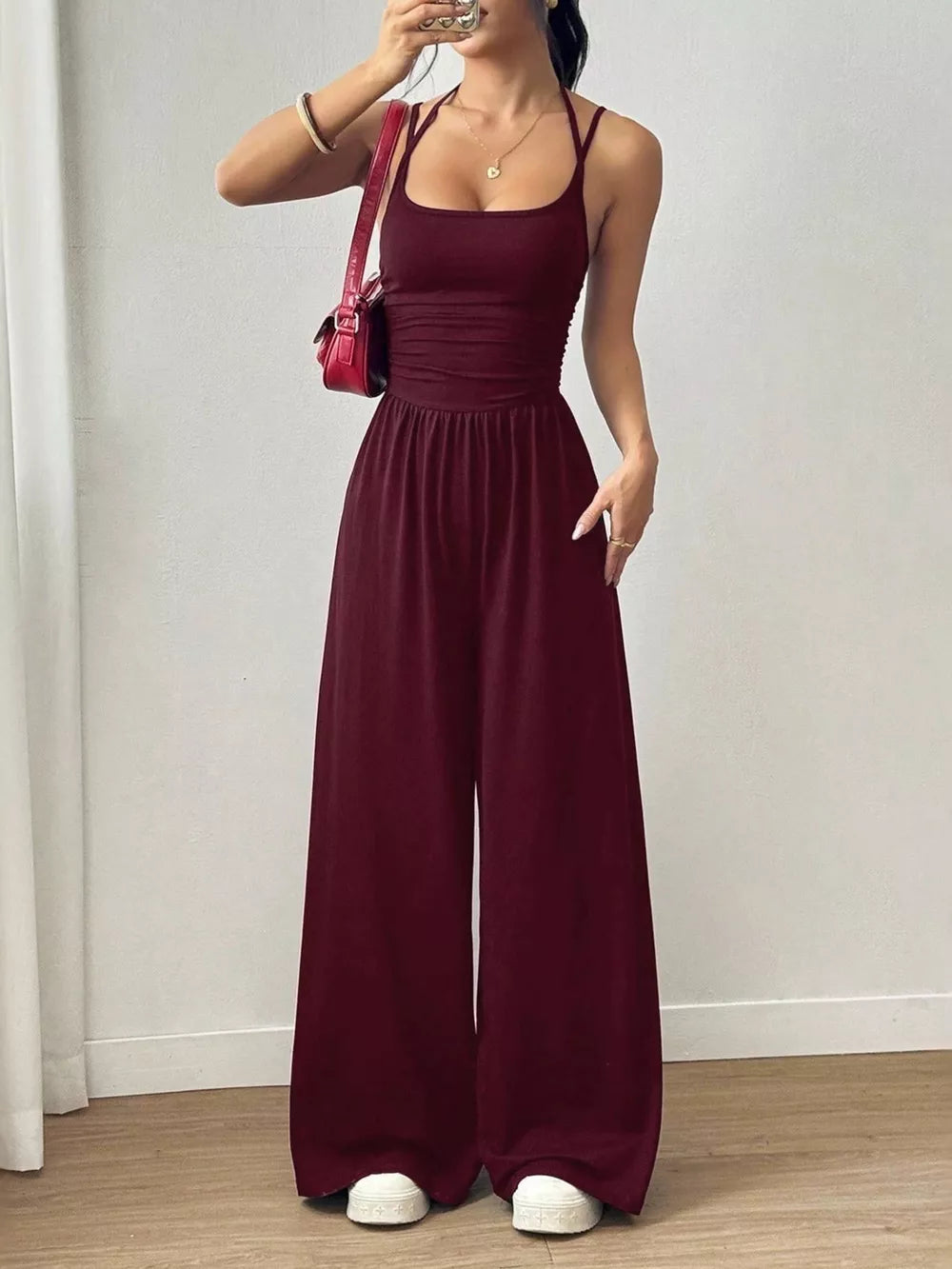 Burgundy ruched wide-leg jumpsuit with spaghetti straps and square neckline.