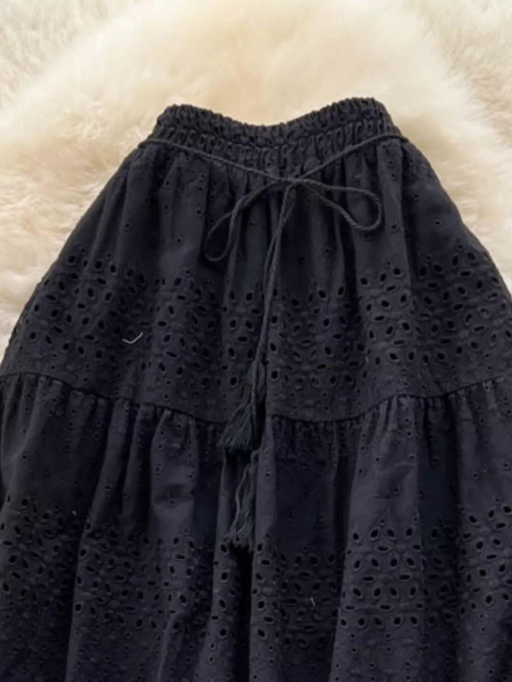 Black eyelet tiered maxi skirt with drawstring waist and tassel detail.