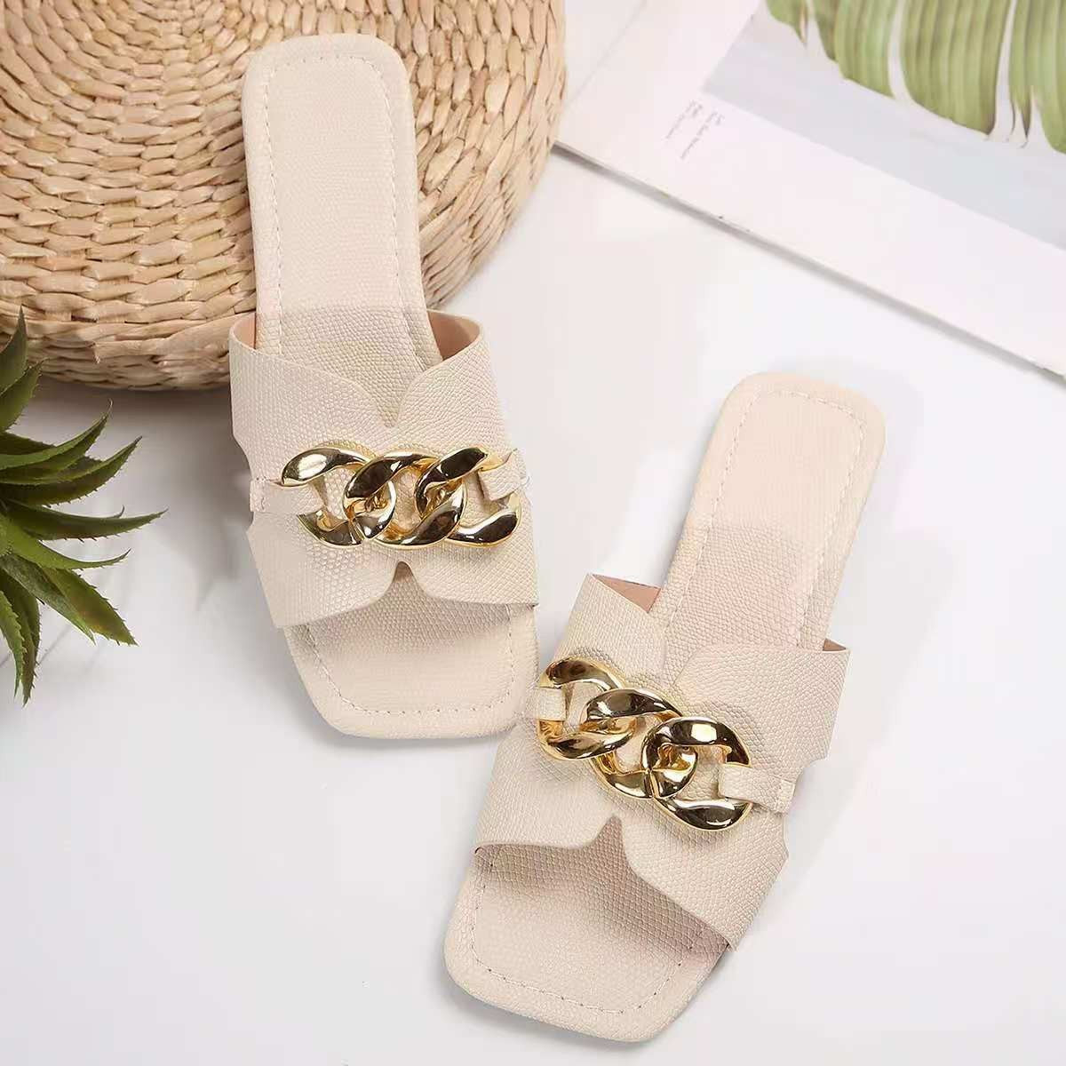 White slide sandals with textured straps and gold chain embellishment.