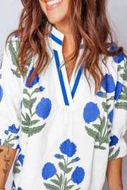 White cotton blouse with blue floral print, ruffled sleeves, and notched neckline.