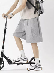 Men's grey sweat shorts with drawstring and curved pockets, styled with a t-shirt and sneakers.
