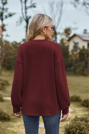 Burgundy textured cable knit V-neck sweater with long sleeves and a relaxed fit.