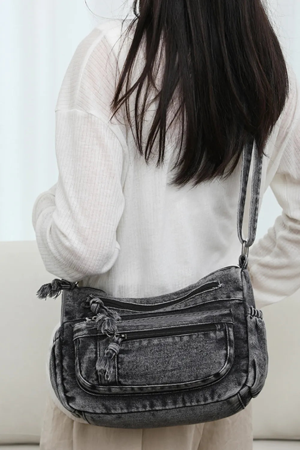 Acid wash denim crossbody bag with multiple zippered pockets and tassel details.