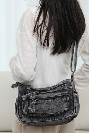 Acid wash denim crossbody bag with multiple zippered pockets and tassel details.