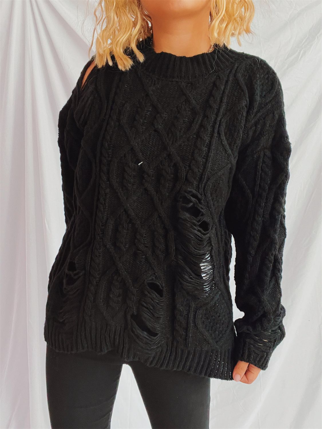 Black distressed cable knit sweater with ripped details and cut-out shoulder.