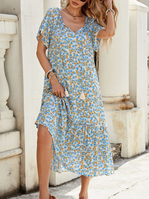 Blue midi dress with daisy print, tie-front neckline, flutter sleeves, and tiered hem.