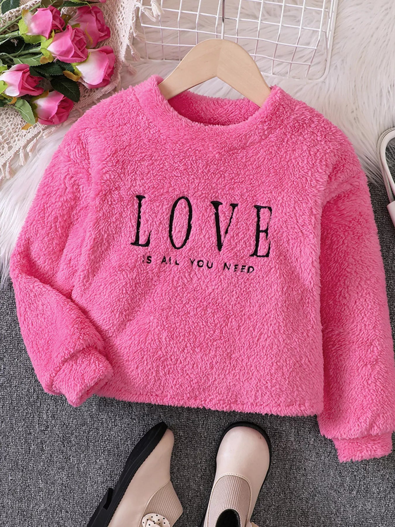 Fuzzy pink sweatshirt for kids with black "LOVE IS ALL YOU NEED" graphic.