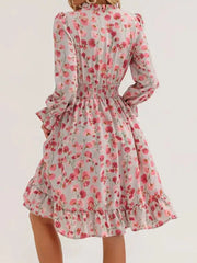 Romantic floral smocked dress in blush pink with ruffled hem and long sleeves.