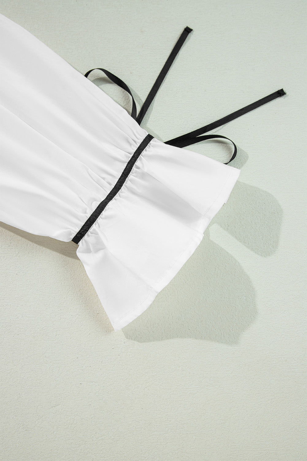 White blouse with black piped trim and tie detail on sleeve cuff