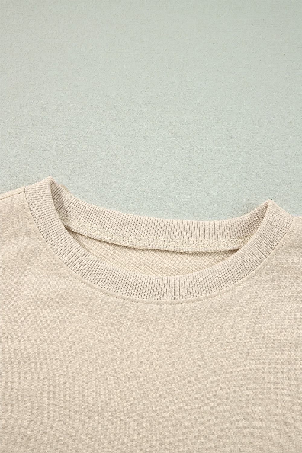 Cream sweatshirt with ribbed crew neck and visible stitching detail.