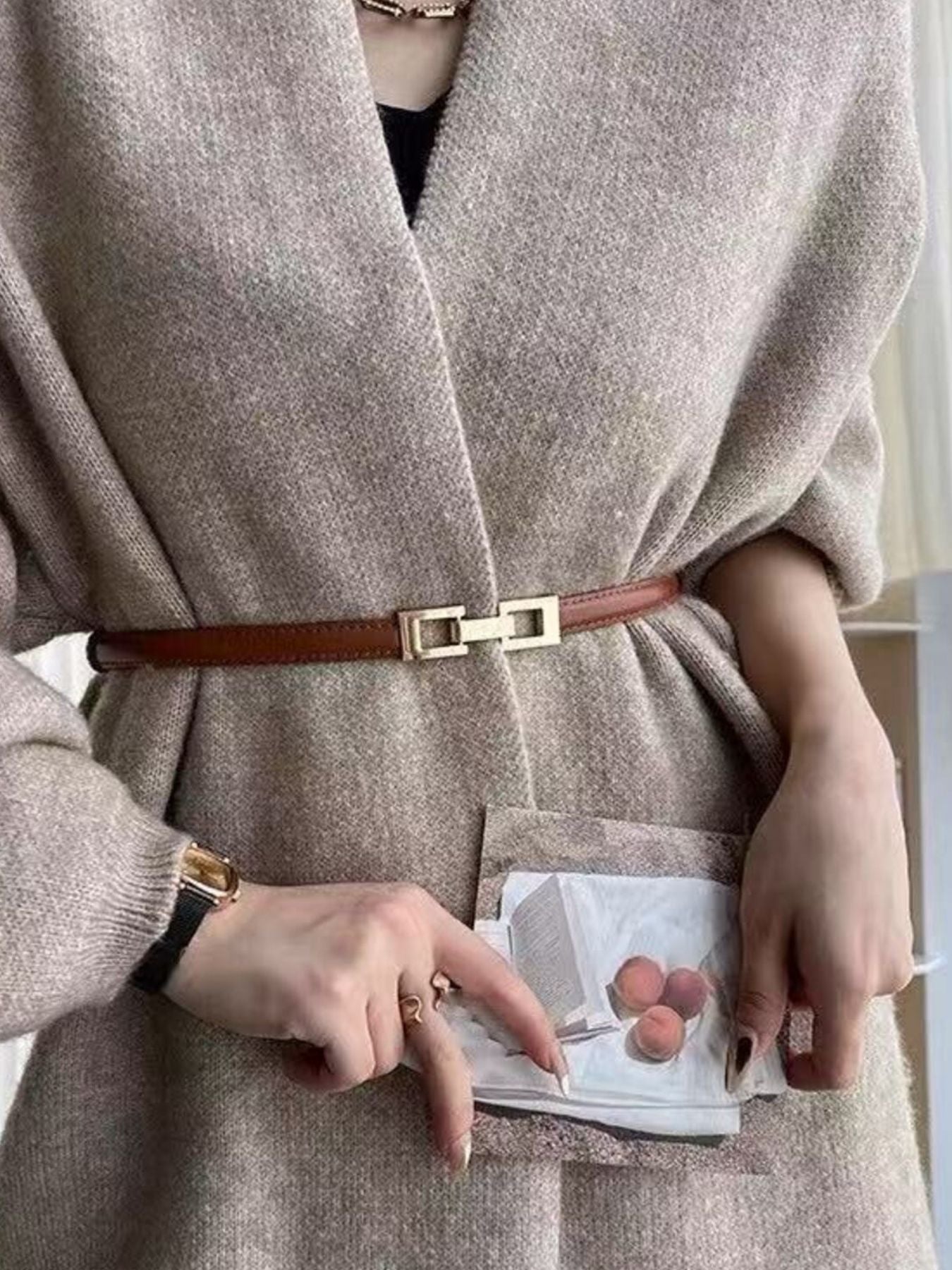 Brown cowhide leather belt with a gold buckle cinched over a tan cardigan.