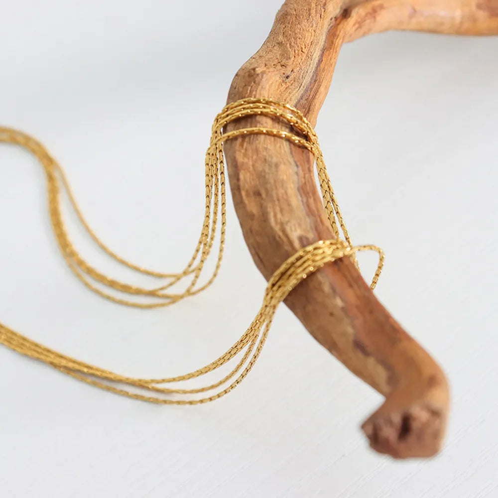 Delicate gold multi-strand collar necklace with fine chains wrapped around wood.