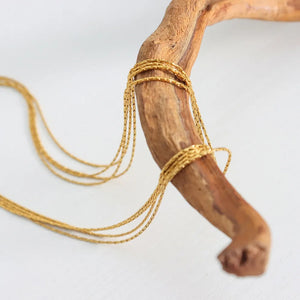 Delicate gold multi-strand collar necklace with fine chains wrapped around wood.