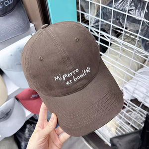 Brown baseball cap with white embroidered "Mi perro es boniti" text and paw prints.