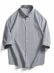 Grey cotton oversized button-down shirt with white vertical stripes and buttoned cuffs.