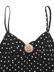 Black polka dot spaghetti strap dress with ruched bust and gold flower detail.
