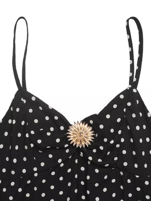 Black polka dot spaghetti strap dress with ruched bust and gold flower detail.
