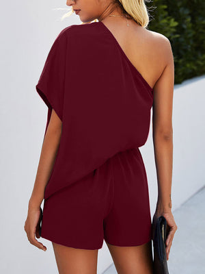 Burgundy asymmetric drape playsuit with elastic waist and one shoulder.