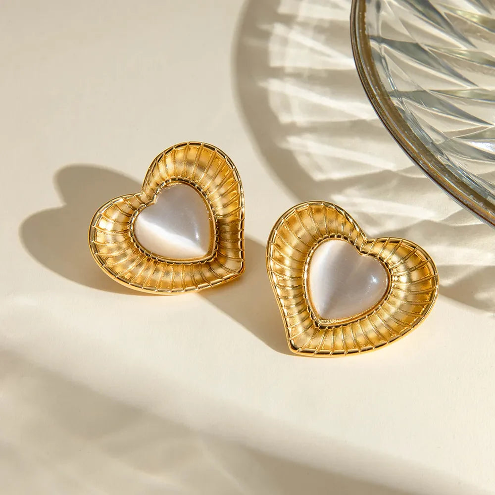 Golden heart cabochon stud earrings with ribbed gold frames and iridescent white centers.