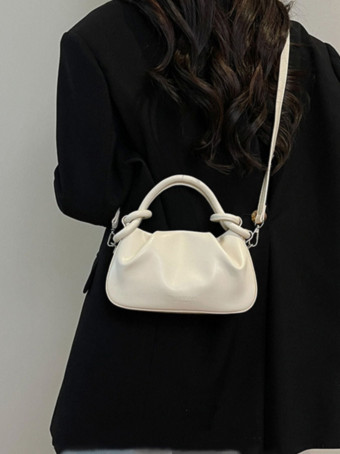 Off-white ruched crossbody bag with knot handle and adjustable strap.